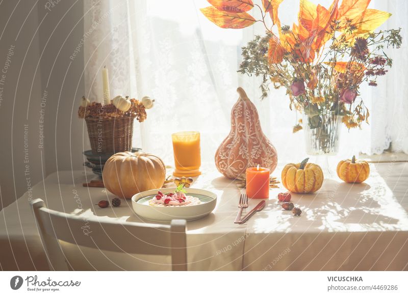 Autumn breakfast table with pumpkins, bunch of orange fall leaves and flowers, waffles with whipped cream and candles. Domestic still life at window with sunlight