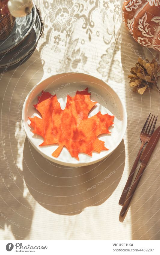 Orange maple leaf decoration on plate. Autumn table setting with sunlight and cutlery. Top view autumn top view orange cozy elegant home stylish empty