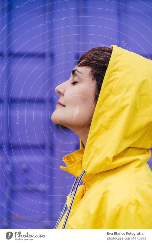 close up portrait of relaxed caucasian woman wearing yellow raincoat, standing with eyes closed over purple background. Lifestyle outdoors side view back view