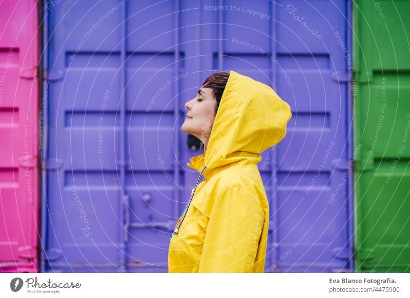 portrait of relaxed caucasian woman wearing yellow raincoat, standing with eyes closed over purple background. Lifestyle outdoors side view back view colorful