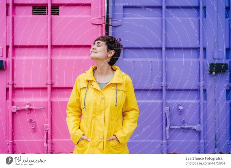 portrait of relaxed caucasian woman wearing yellow raincoat over pink and purple background. Colorful Outdoors lifestyle colorful outdoors city urban beautiful