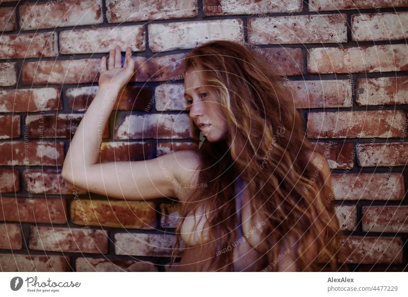 Portrait of a naked young woman with freckles and red hair pausing in a dancing pose in front of a brick wall portrait Near proximity Emanation tranquillity