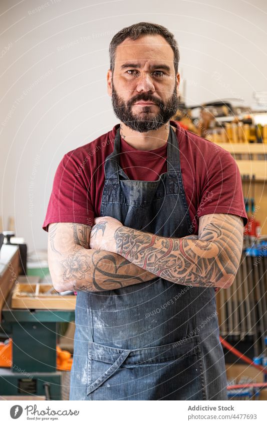 Male in apron standing with crossed tattooed arms in workshop man master professional equipment instrument arms crossed positive male adult small business