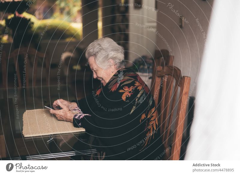 Aged woman with gadget sitting at table tablet at home tea device pensioner senior elderly aged drink browsing using female cup smile warm toothy smile retire