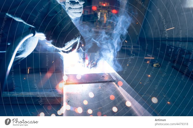 Welder welding metal with argon arc welding machine and has welding sparks and smoke. Man wear protective gloves. Safety in industrial workplace. Welder working with safety. Steel industry technology.