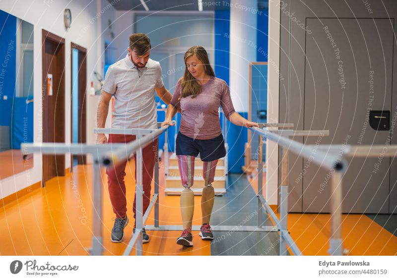 Young woman walking with prosthetic limbs being assisted by male physiotherapist physiotherapy determination recovery rehabilitation strength workout legs