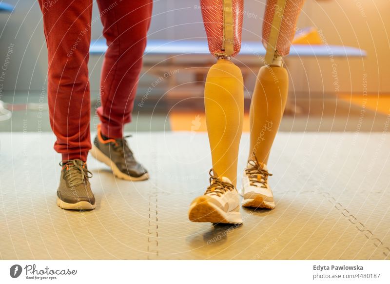 Close-up of a woman walking with prosthetic limbs being assisted by physiotherapist physiotherapy determination recovery rehabilitation strength workout legs