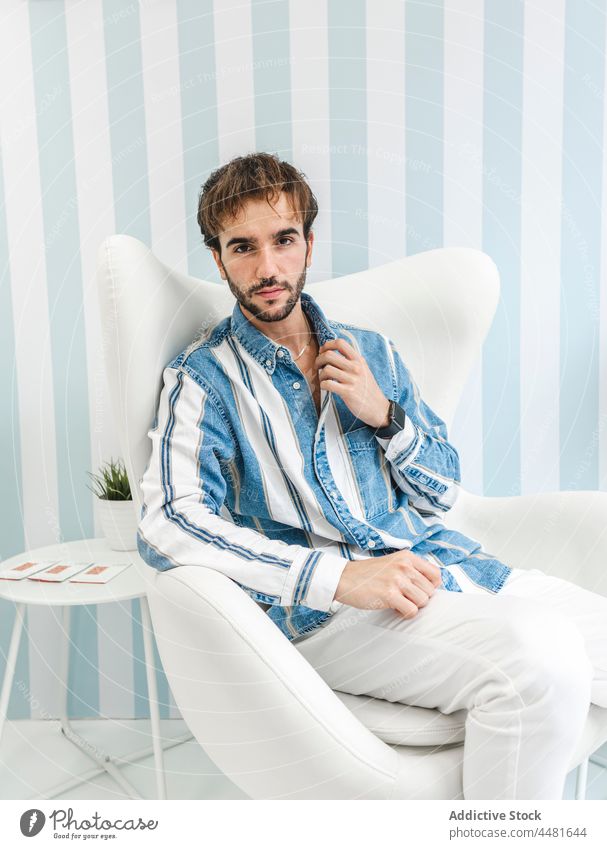 Stylish man sitting on armchair well dressed elegant confident beard charismatic style apparel collar adjust male trendy serious appearance handsome outfit guy