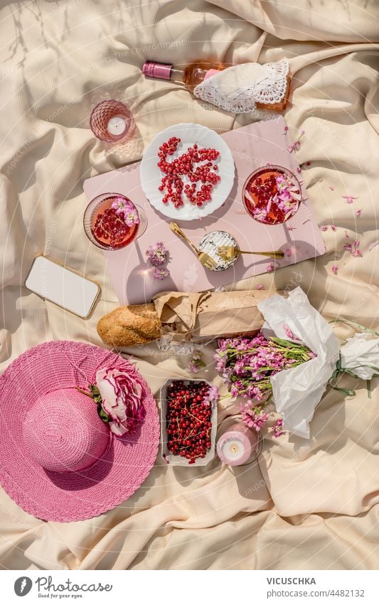 Summer picnic with fresh berries, baguette, rosé wine and glasses, cheese and flowers, pink sunhat and candles on beige cloth. Romantic pink themed brunch concept. Top view.