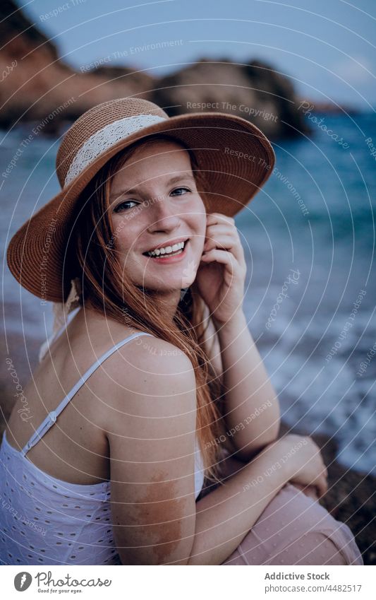 Smiling woman in hat on beach sea summer smile happy water coast nature female shore sit charming young trendy pleasure peaceful glad headwear seaside