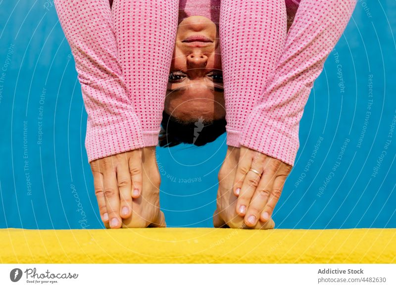 Woman wearing light pink sportswear doing Head to Knees pose woman yoga practice flexible stretch asana uttanasana forward bend wellness wellbeing yellow blue