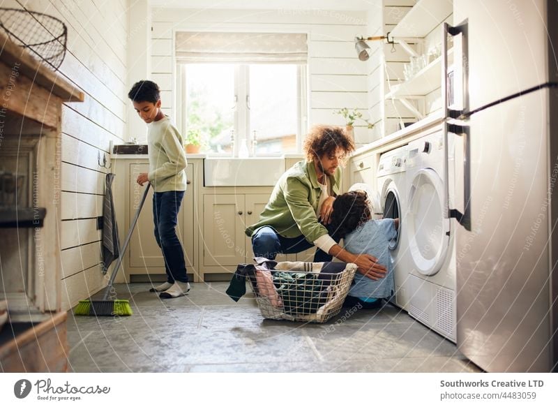 Two boys helping father with household chores mixed race child kitchen sweep broom laundry indoors day home interior three group authentic washing machine