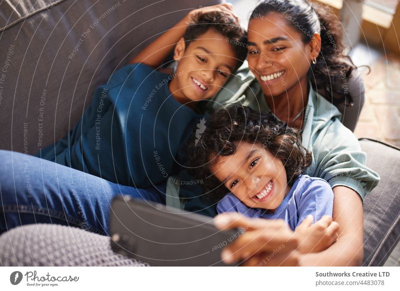 Mother and sons taking selfie on phone mixed race asian mother relax leisure bonding love indoors day home interior three people family portrait authentic