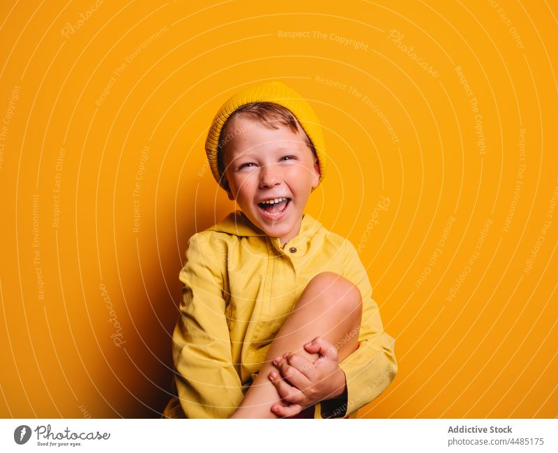 Laughing boy looking at camera against yellow background happy laugh cheerful autumn portrait jacket outerwear beanie glad joy style kid trendy child bright