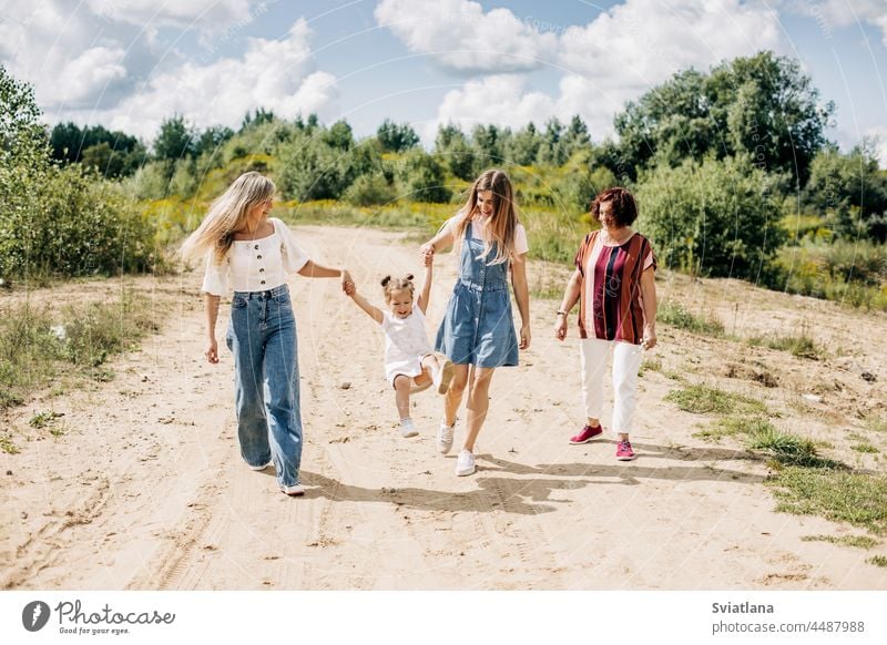 Several generations of women of the same family are walking along a dirt road outside the city, enjoying the time spent together grandmother granddaughter
