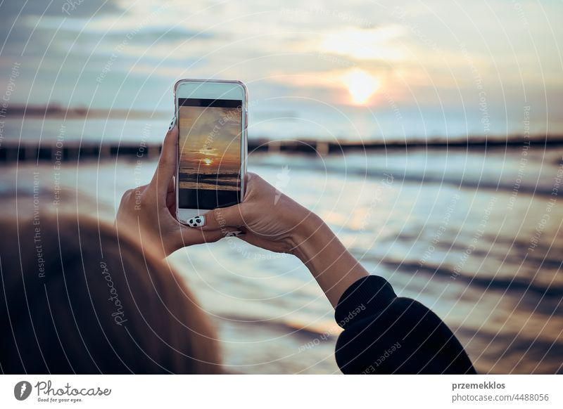 Young woman taking photos of sunset over sea using smartphone during summer trip photographer picture technology screen person female holding ocean photography