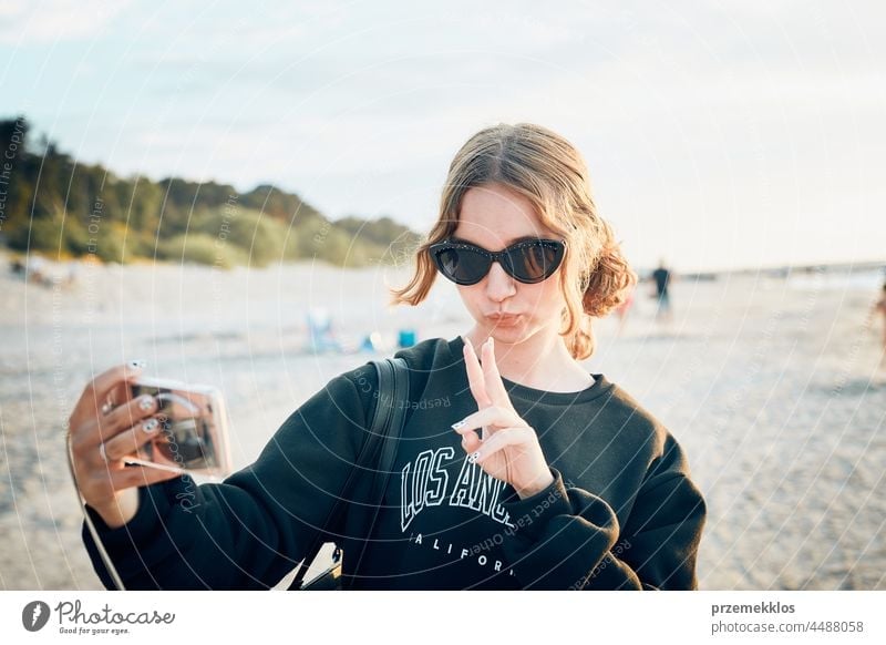 Teenager girl making gesture during video call on smartphone during trip on summer vacation chat greeting taking photo selfie person woman mobile phone holding