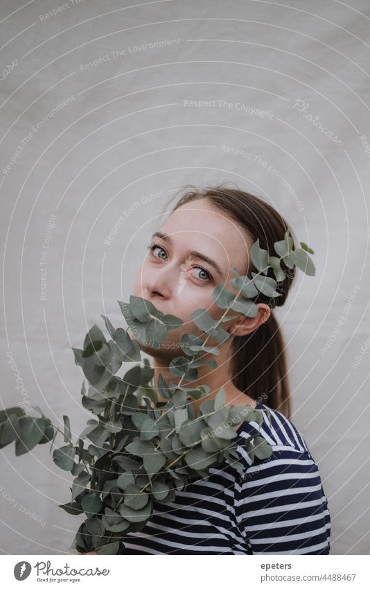 Young attractive woman with a eucalyptus branch looking into the camera in front of a canvas adult background beautiful beauty brunette caucasian closeup