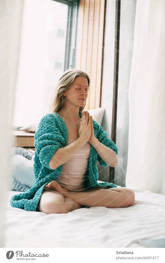 A young girl meditates while sitting in the Lotus position on the bed in the bedroom. The girl does anti-stress yoga in the morning at home meditation woman