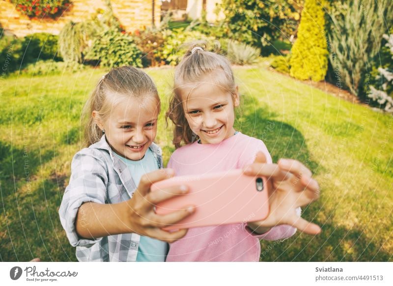 Two happy teenage girls laugh and take a selfie on a cell phone outdoors. kids smartphone adoption people education school leisure gadget technology group soda