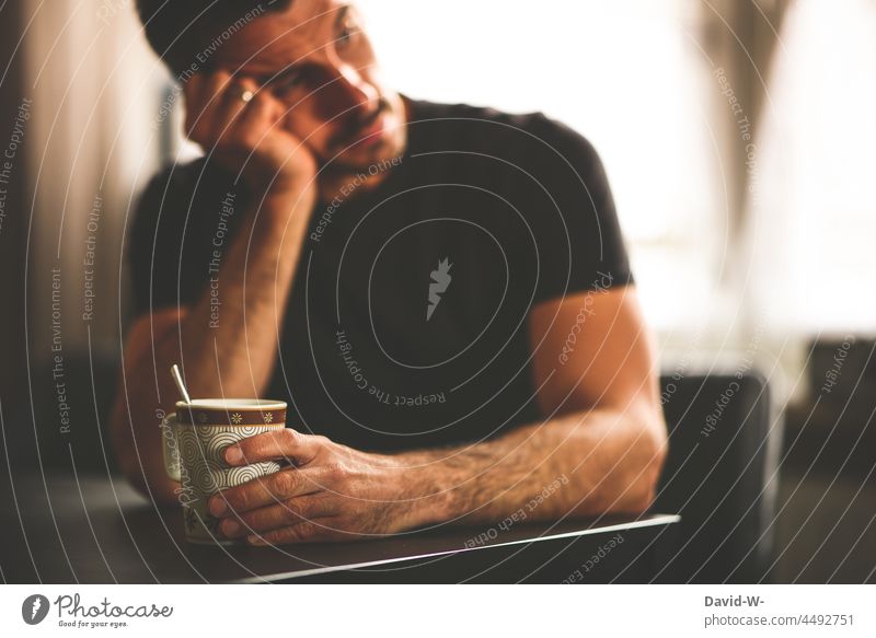 thoughtful man sits at the table and holds a coffee mug in his hand Meditative Man Think thoughts Fear of the future Doubt Exhaustion Coffee break