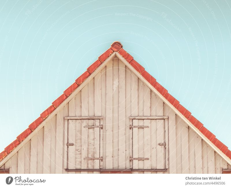 House gable with wooden facade and two closed doors in front of pale blue sky pediment house gables Gable Wooden facade Pointed gable locked too Hinges Facade