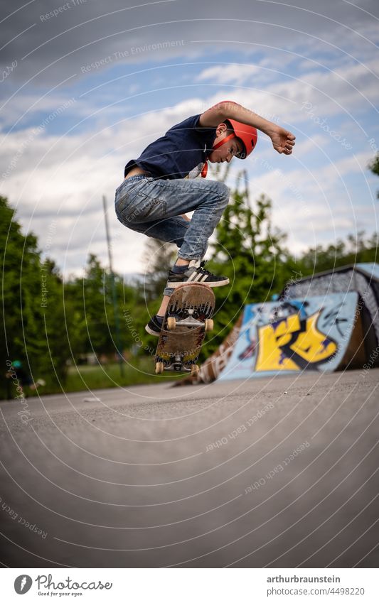 Boy in jeans and helmet does an ollie in outdoor skatepark Boy (child) daylight Asphalt Movement cloudy board boardsport Cool deck free time graffiti Halfpipe
