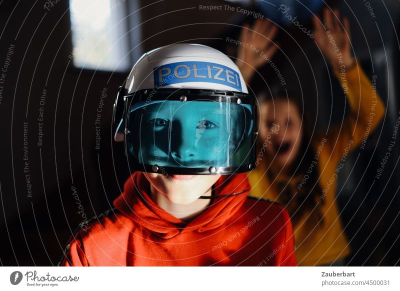 Boy with police helmets and blue visor, behind him a girl Boy (child) Police Force Gun sight Blue Girl Scare game children Infancy fun Playing free time Red