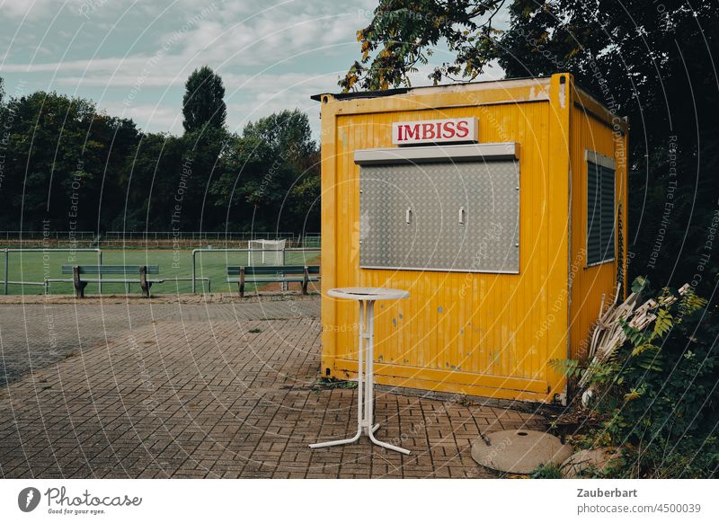 Yellow snack container on sports field with bar table has closed Snack bar Container Sporting grounds high table Closed Nutrition Eating Empty forsake sb./sth.