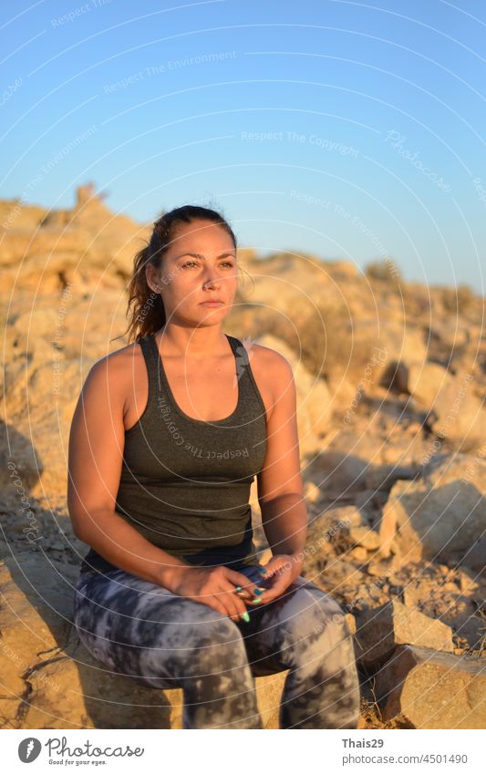 A young traveler girl sit on the top of mountain in Negev desert and enjoy the beauty of nature. Young girl love wild life, travel, freedom. A girl sits on the edge of the cliff and looking at the sun