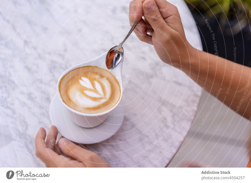 Crop person holding spoon above cup of latte coffee latte art mug beverage hot drink table tasty caffeine delicious aromatic creative design cafeteria portion