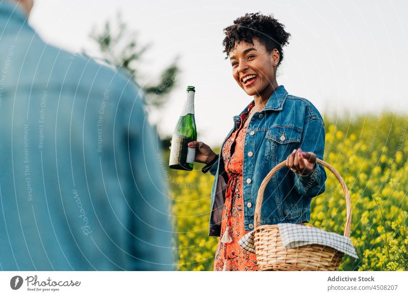 Happy ethnic woman with champagne bottle smiling with crop boyfriend in park couple love cheerful celebrate nature happy romantic together date positive picnic
