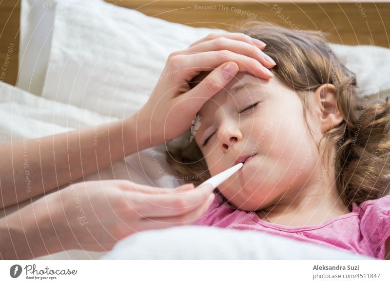 Mother measuring temperature of her ill kid. Sick child with high fever laying in bed and mother holding thermometer. Hand on forehead. sick flu little girl