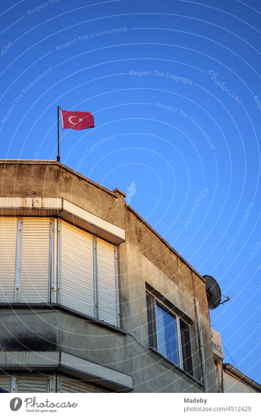 Old facade of a corner house with lowered blinds and or Turkish flag against a blue sky in the light of the evening sun in Foca on the Aegean Sea in Izmir province, Turkey