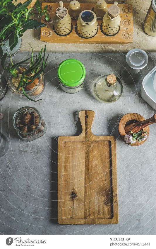 Food background with wooden cutting board, mortar and pestle, jars with ingredients and herbs at grey kitchen table. Cooking at home with plastic free kitchen utensils. Top view with copy space.