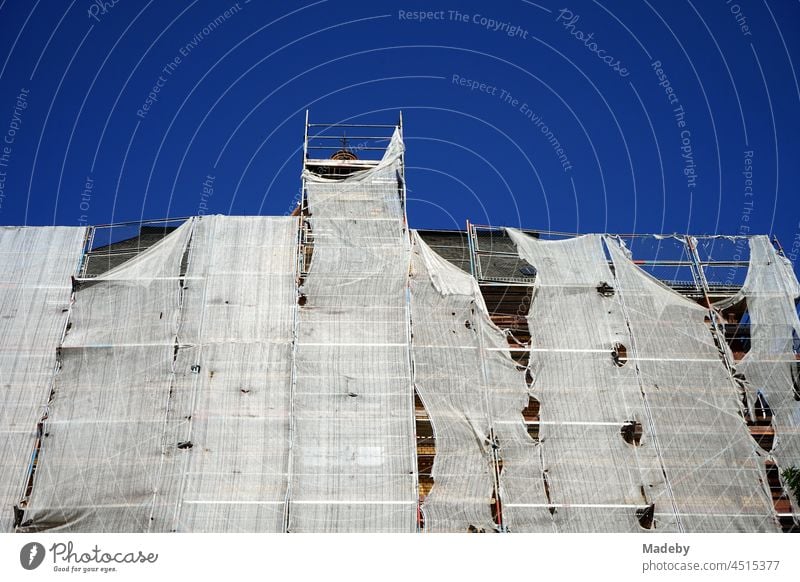 Scaffolding with tattered safety net during the renovation of the facade of a large old building in front of a blue sky in sunshine in the district of Sachsenhausen in Frankfurt am Main in the German state of Hesse