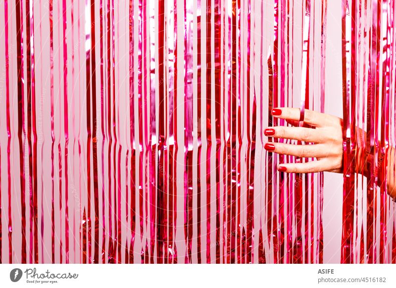 Beautiful woman hand with nail polish in red breaking through a pink tinsel party curtain beauty fashion foil glitter new year shimmer retro glow shine