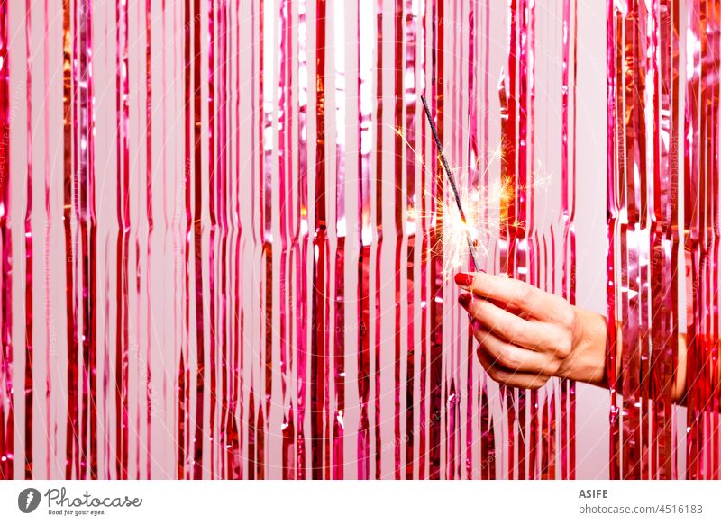 Woman hand  breaking through a pink tinsel with a burning sarkler. sparkler woman party curtain new year foil glitter shimmer retro red glow shine background