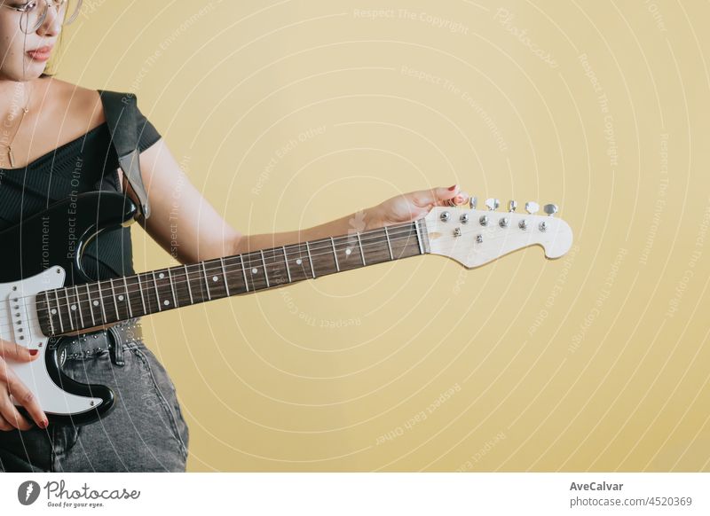 Conceptual studio image of a detail of a woman getting ready to play a electric guitar, yellow background, removable background, banner design, social network advertising, copy space