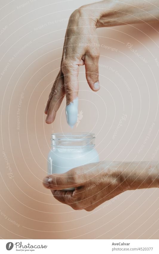 Old hands taking body lotion cream from a bottle, minimalist shot, pastel colour background skin skin care applying skincare routine purity cosmetic female
