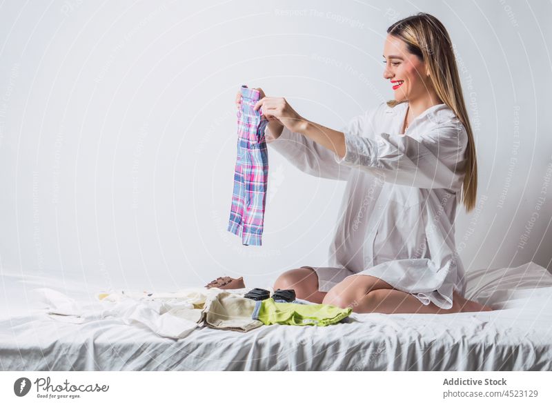 Pregnant woman in white shirt preparing baby clothes pregnant fold expect prenatal anticipate prepare wait pregnancy female crumple kid motherhood bed wear