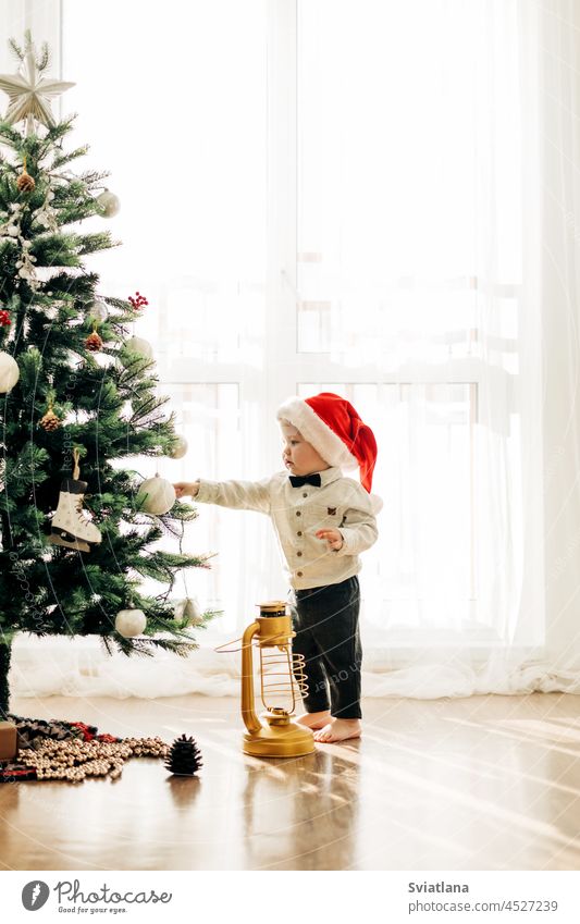 A little kid in a Christmas hat on the background of a Christmas tree. Christmas themed picture, postcard. baby boy christmas christmas hat christmas tree