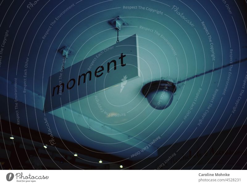 Sign reading "Moment" hangs from a ceiling in an alleyway instant sign Lamp Signs and labeling Signage Clue Deserted Characters Exterior shot Letters (alphabet)