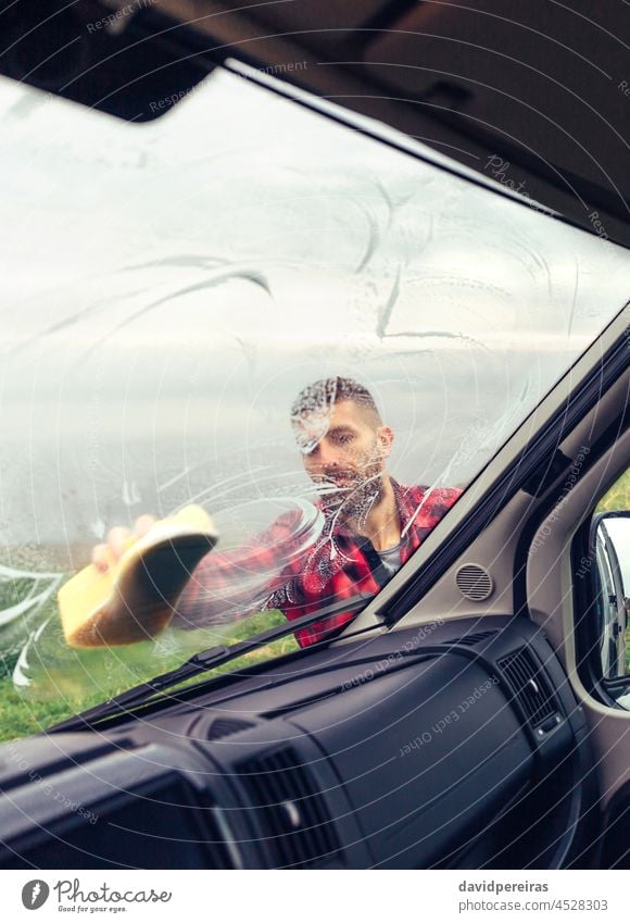 Man cleaning motorhome glass outdoor young man soaping window sponge view from inside through the glass outdoors windscreen careful owner perfectionist rub