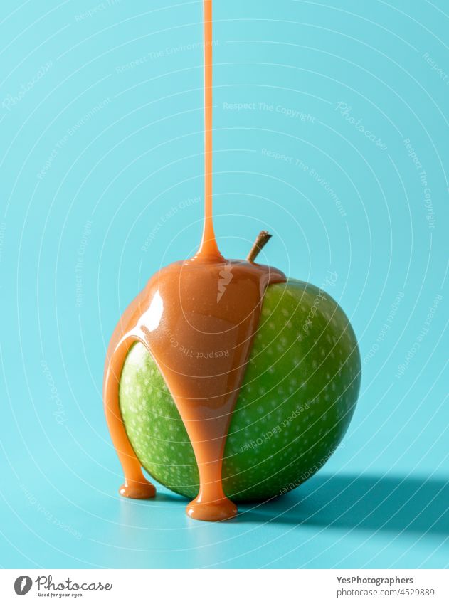 Caramel apple on blue background. Pouring caramel sauce on green apple brown calories candy christmas close-up color condensed cream cuisine cut out delicious