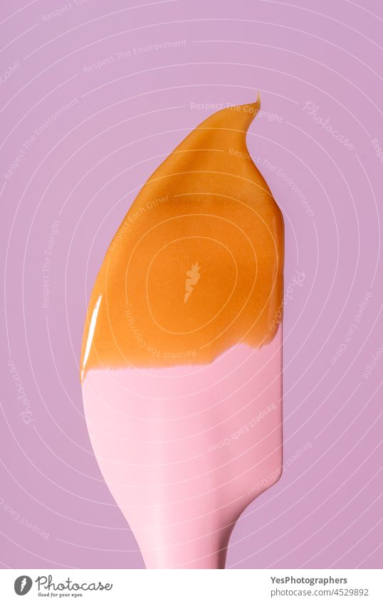 Caramel sauce dripping on a silicon spatula, minimalist on a pink background. bake brown calories caramel christmas close-up color condensed cooking cream