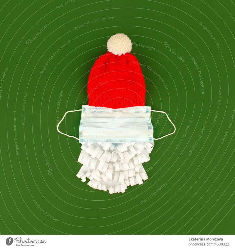 Santa Claus hat and paper beard with medical  face mask on classic green background, creative minimal concept of Christmas and New Year 2022, covid-19 lockdown, new normal