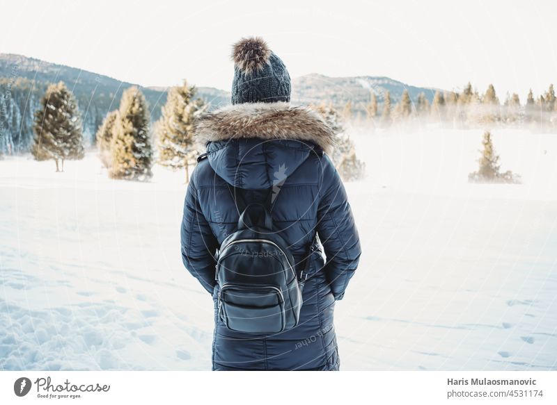 Woman traveling in snow adventure in hat turned back looking at snow mountain active background backpack beautiful blue calm casual caucasian cold copy space