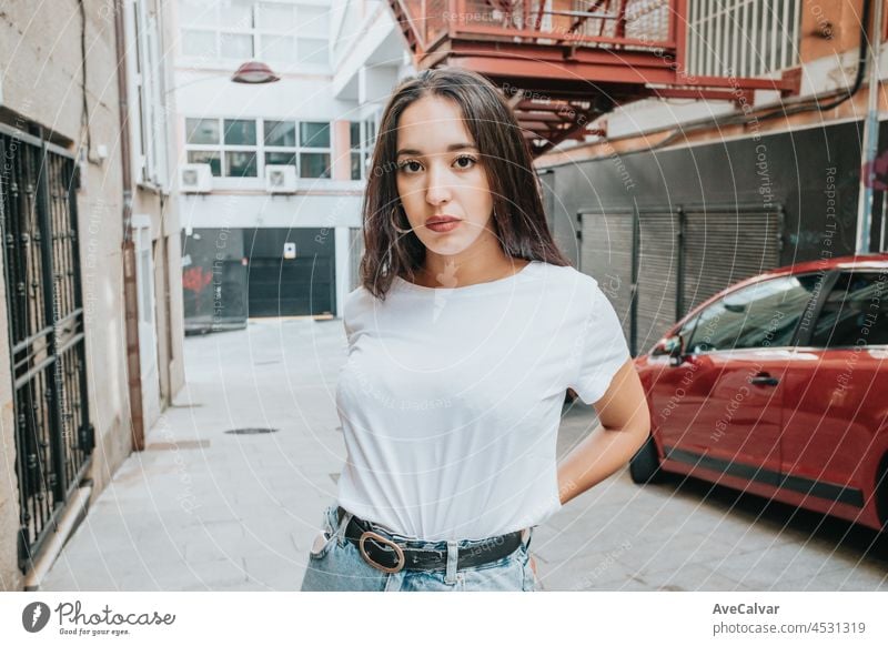 Young urban mixed race woman portrait looking serious to camera, urban lifestyle, white tshirt blank space, model in the hood young confident outside modern