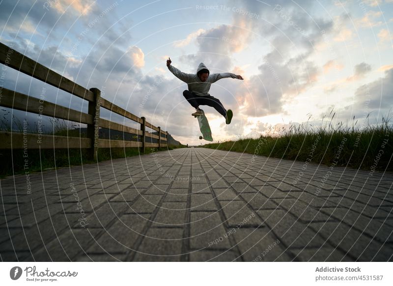Active man jumping on longboard on paved path stunt hobby skill leisure activity freestyle cool male practice trick walkway pavement active motion action